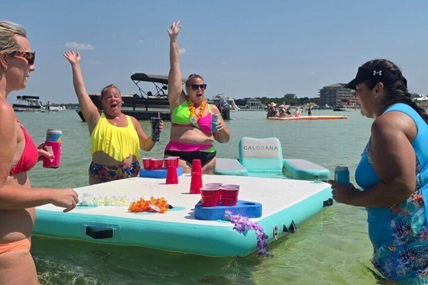 A group of people on a small inflatable boat with drinks and snacks, surrounded by water and distant boats. 2