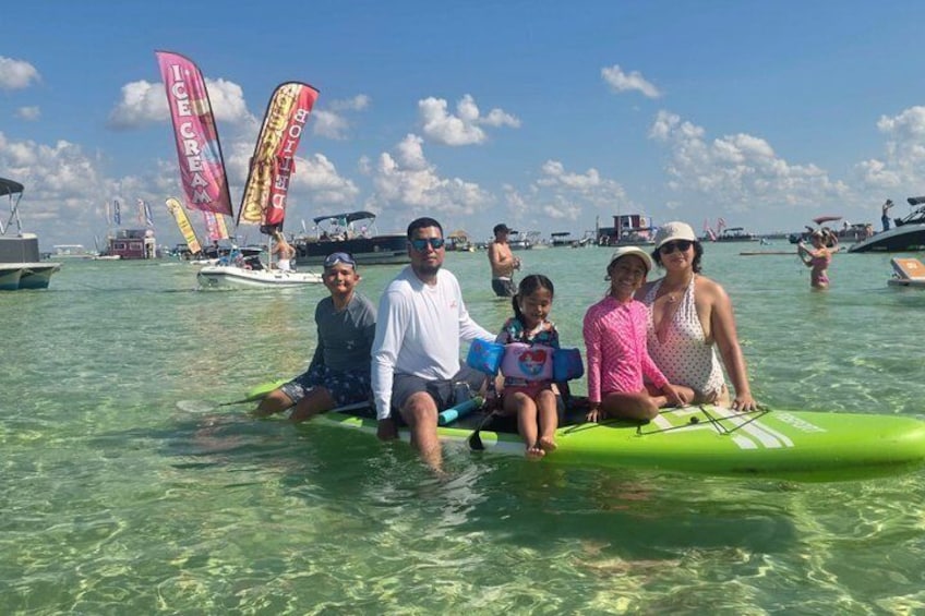 A group of people on a green raft in clear water with sailboats in the background. 5