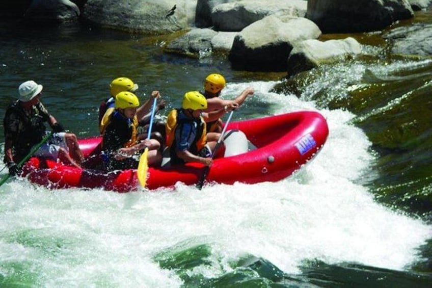 A group of people in a red inflatable raft navigating a river with rapids. 1