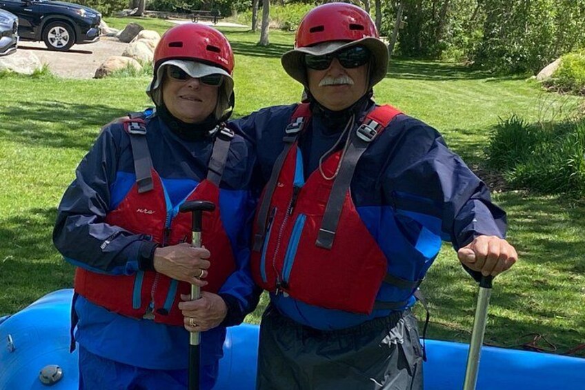 Two people in blue and red life jackets standing next to a blue raft. 3