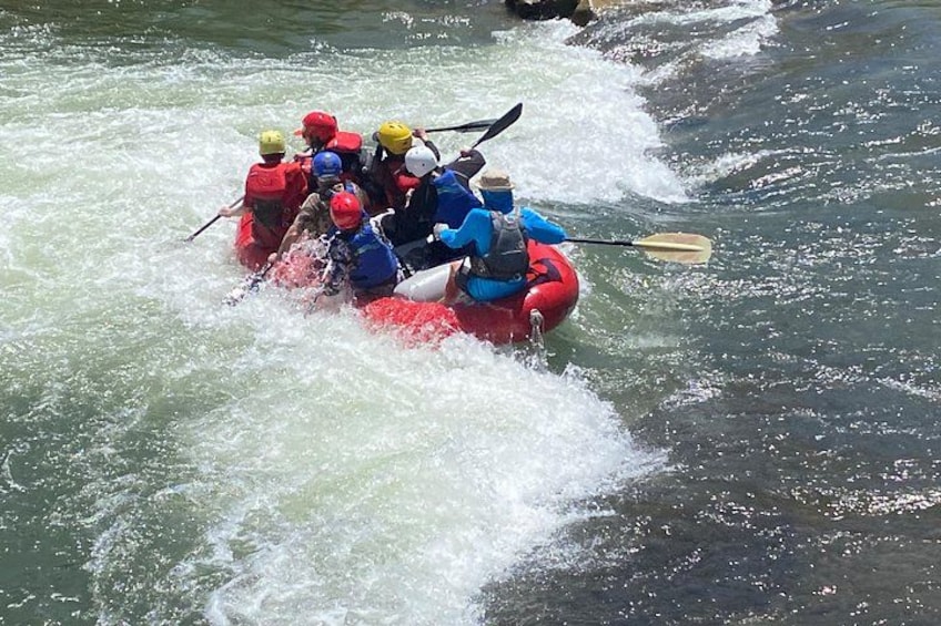 A group of people in a red raft navigating through a river with rapids. 2
