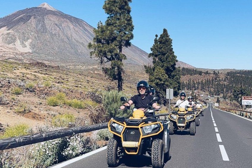 Un groupe de personnes conduisant des quads sur une route, avec une montagne en arrière-plan. 1