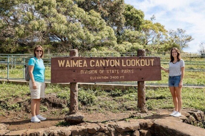 Un letrero del mirador del Cañón Waimea con dos personas a su lado. 4