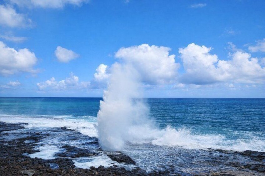 Escena costera con una ola grande rompiendo sobre una costa rocosa bajo un cielo azul despejado. 2