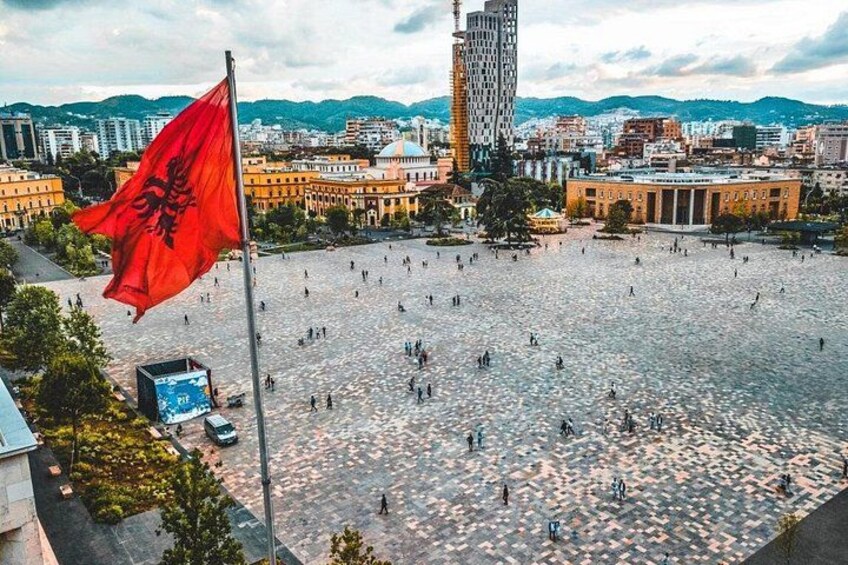 A square with a flag, buildings, and a body of water. 2