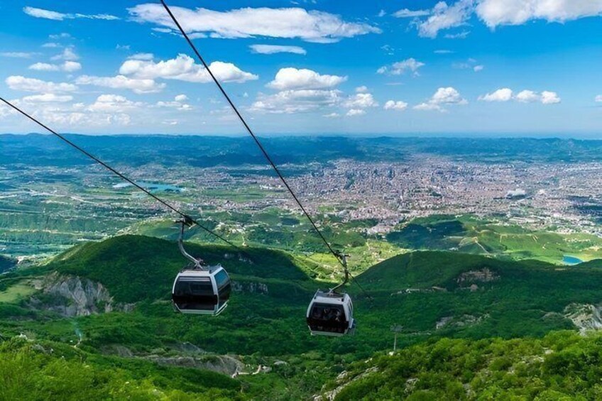 A cable car system with two gondolas over a green landscape and a city below. 3