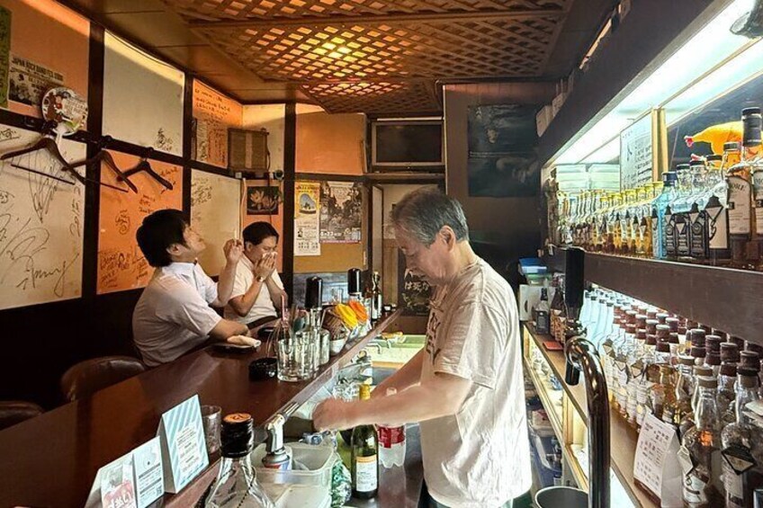 A bar with a bartender preparing drinks. There are bottles and glasses on the counter. 4