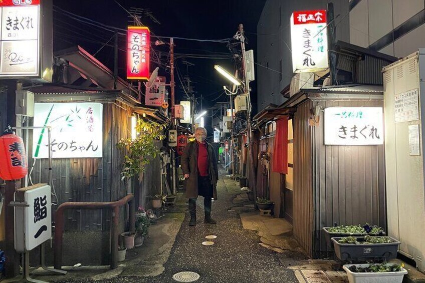 A narrow alley with small shops, signs in Japanese, and a person walking. 2