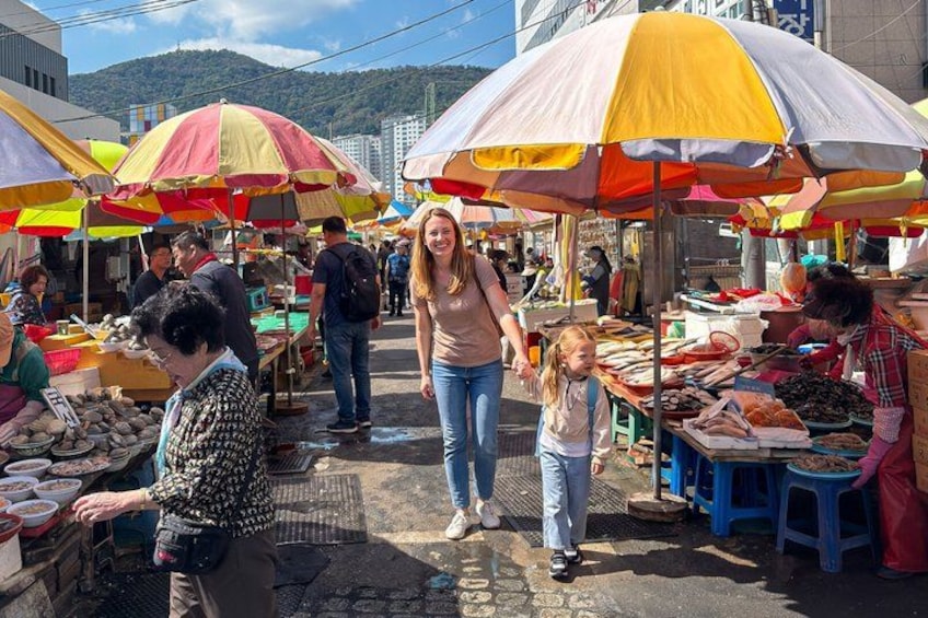 Un mercado al aire libre concurrido, con sombrillas coloridas, gente comprando y diversos productos a la venta. 3