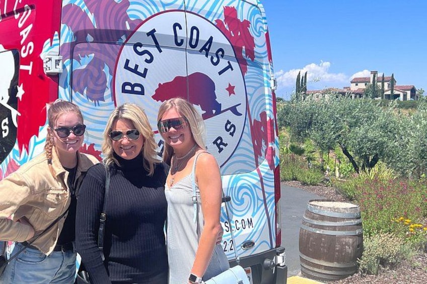 Tres personas posando frente a un letrero con un toro y el texto 'BEST COAST'. 2