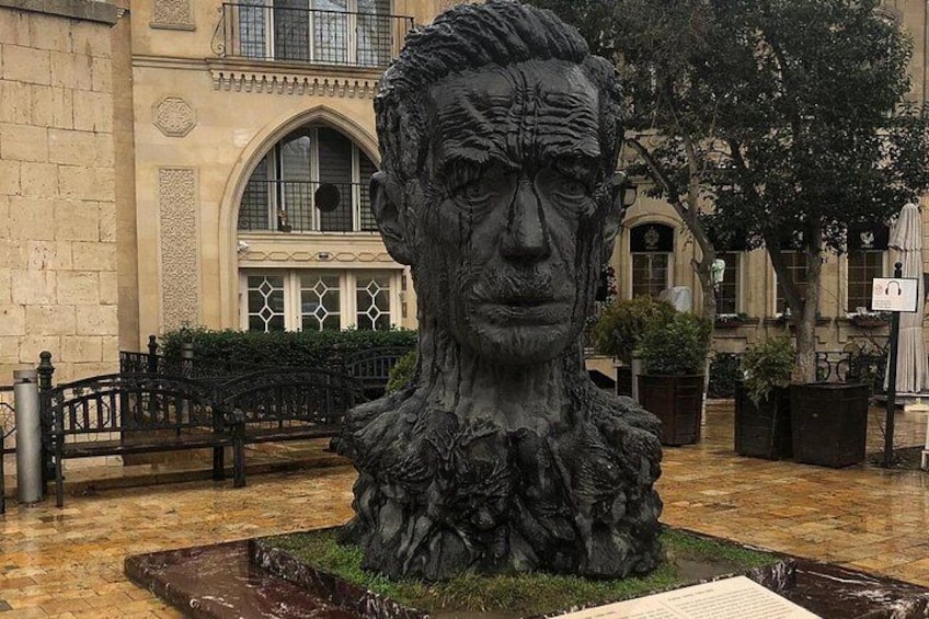 Eine Skulptur in einem Innenhof mit einem Brunnen, umgeben von Gebäuden und einem Baum. 5
