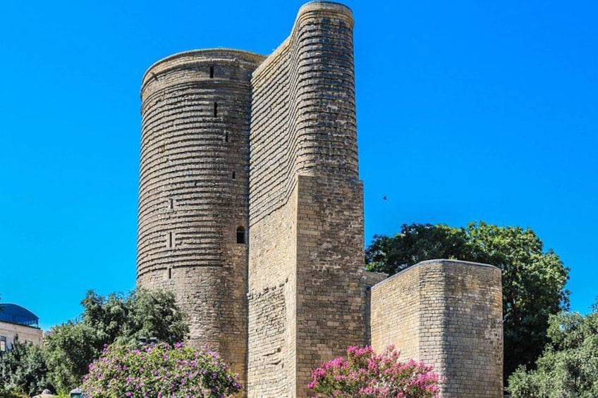Ein historischer Steinturm mit zylindrischer Form und rechteckigem Fundament, umgeben von Grünpflanzen und Blumen. 5