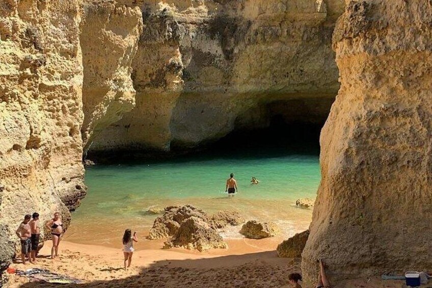 A beach with clear turquoise water, rocky cliffs, and people sunbathing. 2