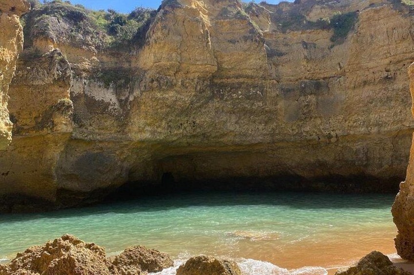A coastal cave entrance with clear turquoise water, sandy beach, and rocky cliffs. 5