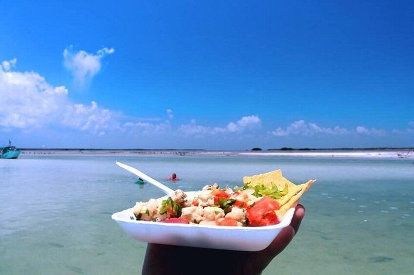 A person holding a plate of food with a clear view of the ocean and a distant shoreline. 3