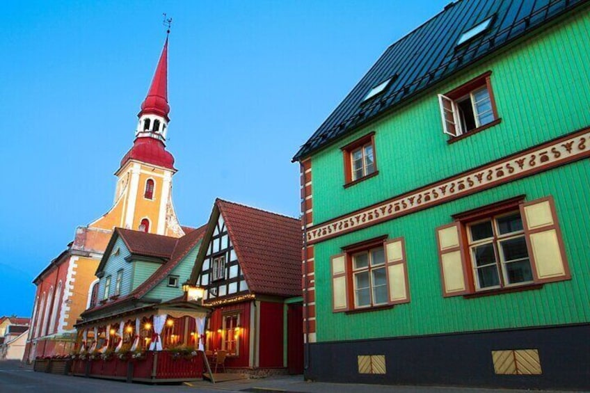 Een kerk met een rode spits, een groen gebouw met een rij ramen, en een vakwerkhuis met een rood dak. 1