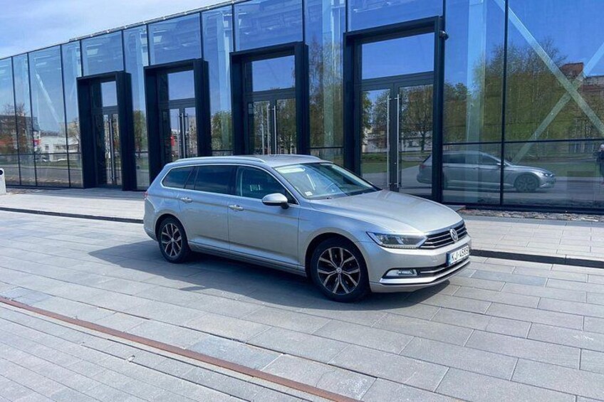 Een zilveren stationwagen geparkeerd voor een modern glazen gebouw. 2