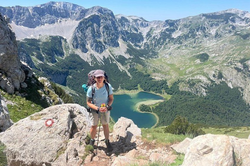 Ein Wanderer auf einem felsigen Vorsprung mit Blick auf einen See, der von Bergen umgeben ist. 5