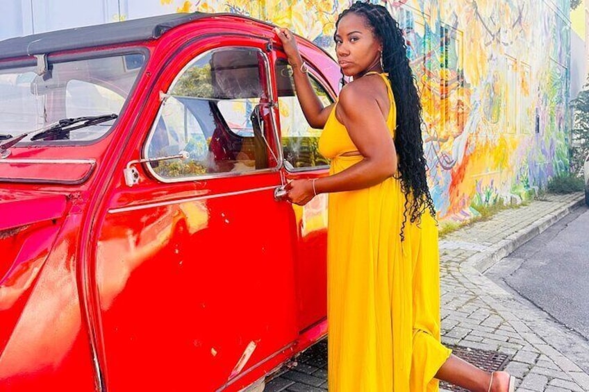 Une femme vêtue d’une robe jaune se tient à côté d’une voiture rouge d’époque. 4