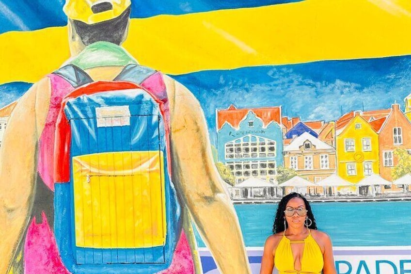 Une personne porte un sac à dos aux couleurs vives devant une fresque murale colorée représentant des bâtiments. 2