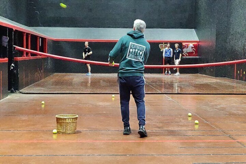 A tennis court with a net, a basket, and tennis balls. 3