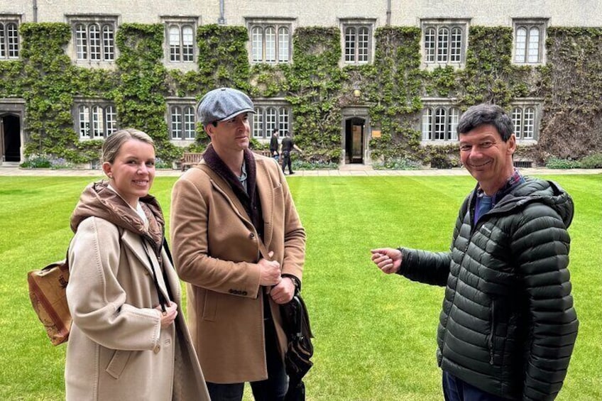 Three people standing in a grassy courtyard with a historic building in the background. 5