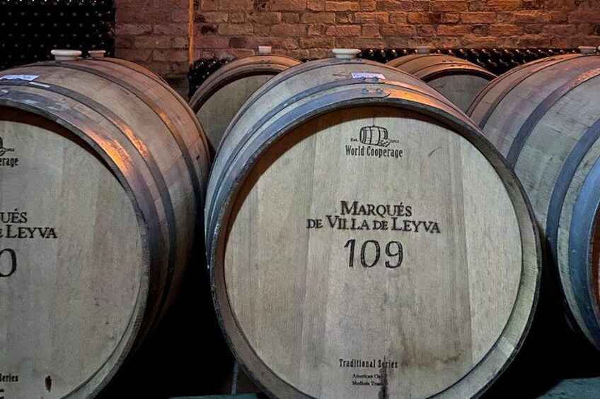 Wooden wine barrels with labels, stacked against a brick wall. 1