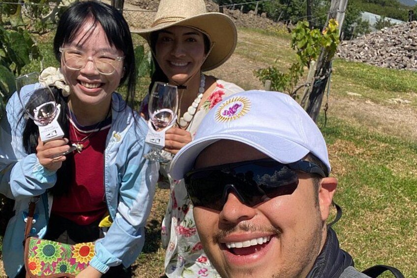 Three people holding wine glasses in a vineyard. 3