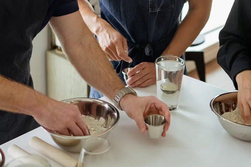 People preparing food, with bowls of ingredients and a rolling pin on a table. 4
