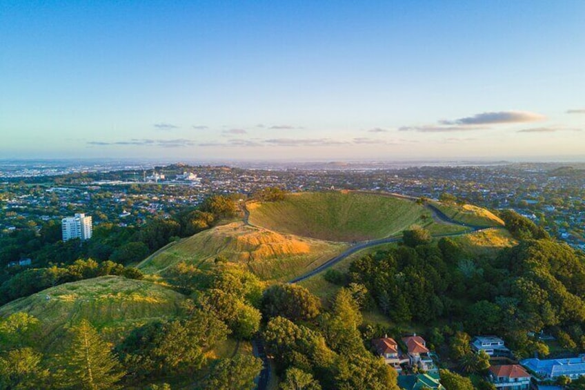 A hilly landscape with a winding road, residential houses, and a distant cityscape. 1