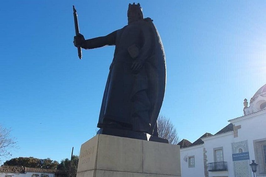 A statue of a figure holding a sword, standing on a pedestal, with a building in the background. 2