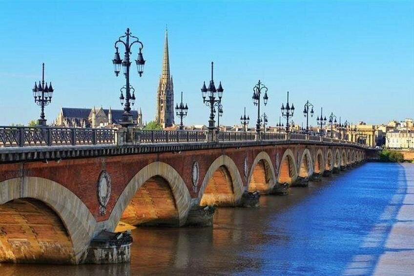 A bridge with multiple arches, a river, and a tall church spire in the background. 4