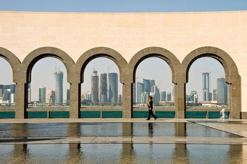 A person walking along a waterfront with arches and a city skyline in the background. 5