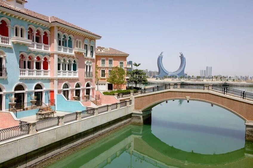 A colorful building with a bridge over a reflective water body, and a large modern sculpture in the background. 4