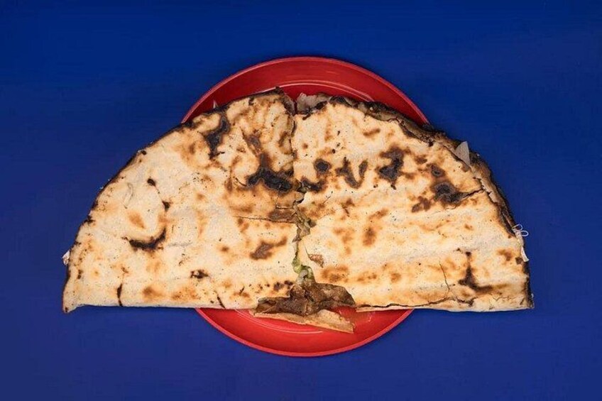 Une galette, parsemée de taches noircies, est présentée sur une assiette rouge, le tout sur un fond bleu. 3