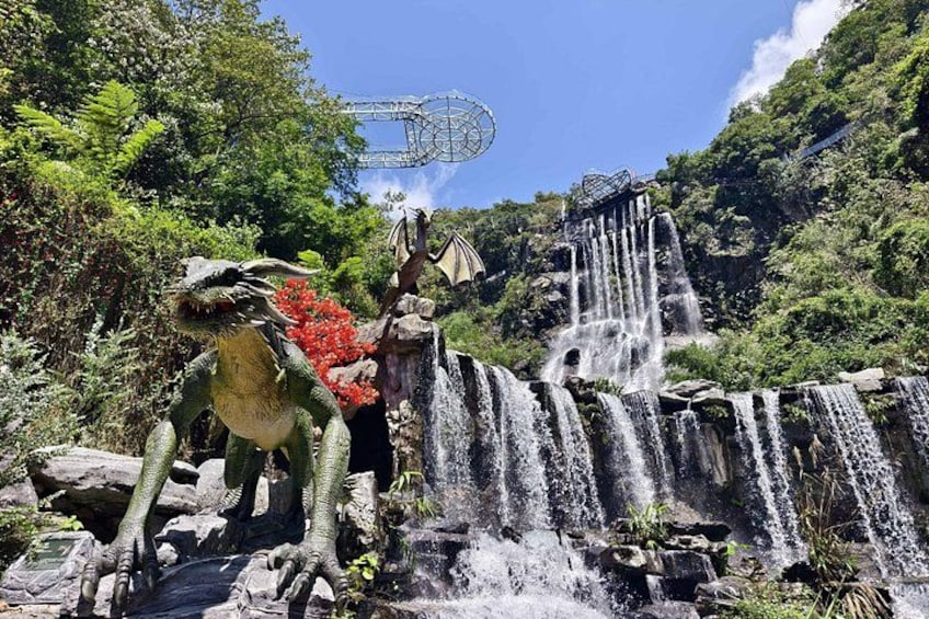A waterfall, a dragon statue, and a roller coaster in the background. 1