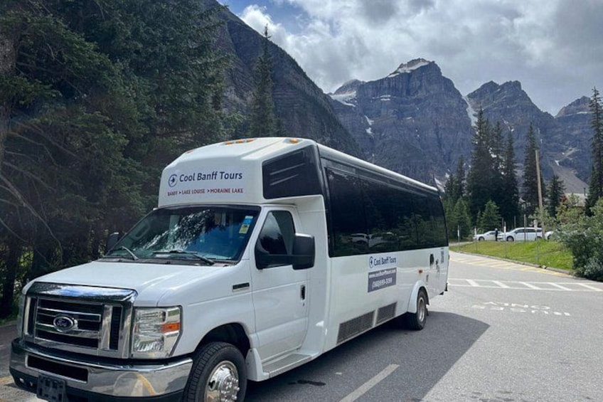 Een witte bus met de branding 'Cool Banff Tours' geparkeerd aan de weg, met bergen op de achtergrond. 5