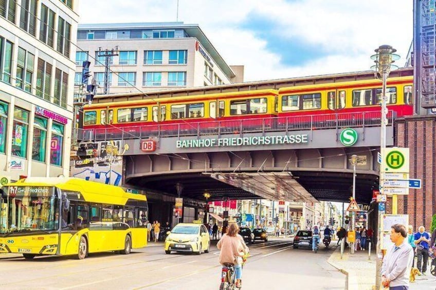 A yellow tram on a bridge over a busy street with pedestrians and cars. 3