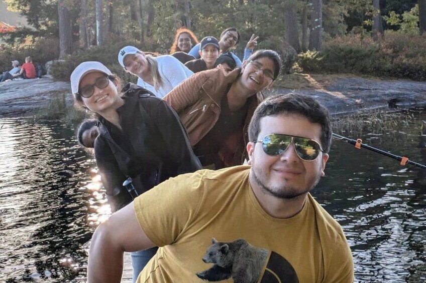 A group of people fishing by a calm river surrounded by trees. 2
