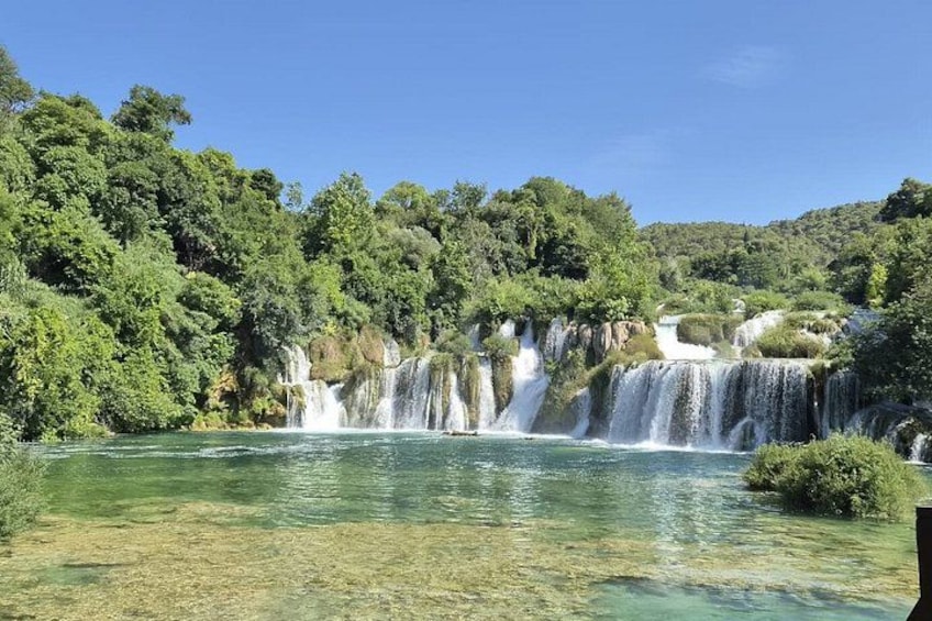 A waterfall cascading into a clear river surrounded by dense forest. 2