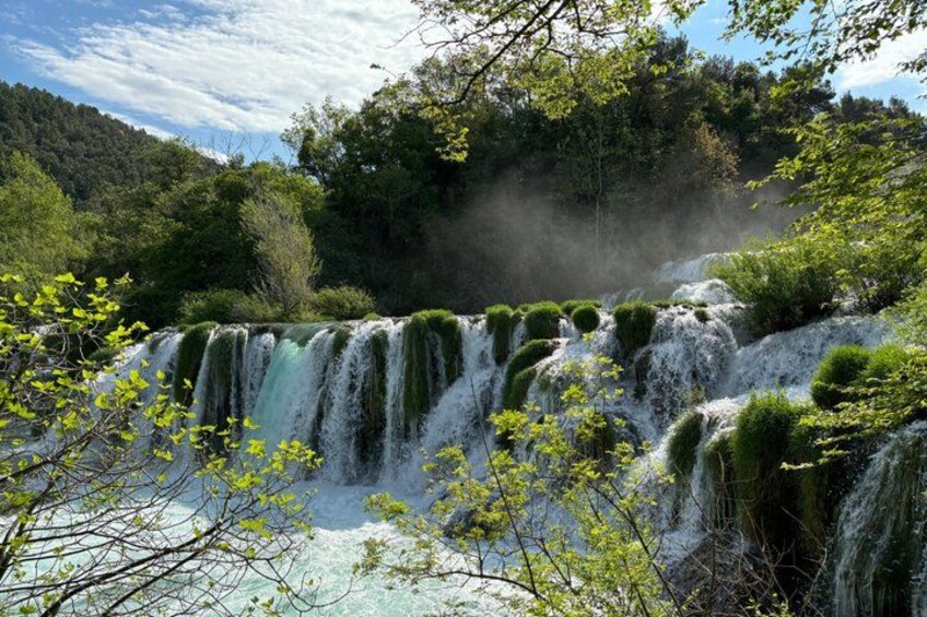 A multi-tiered waterfall surrounded by lush greenery and trees. 1