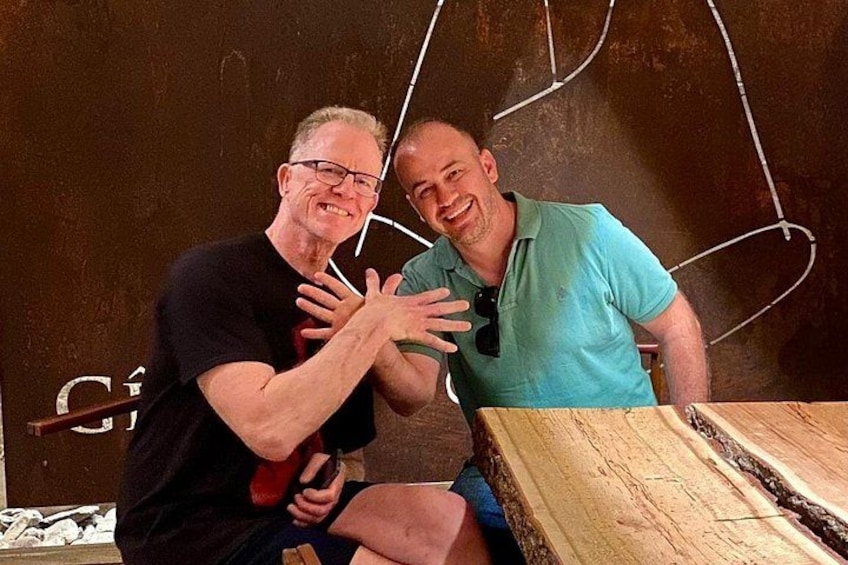 Two men sitting at a table with a large wooden plank. 3