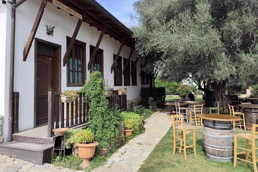A rustic building with wooden beams, a stone pathway, potted plants, and outdoor seating. 5