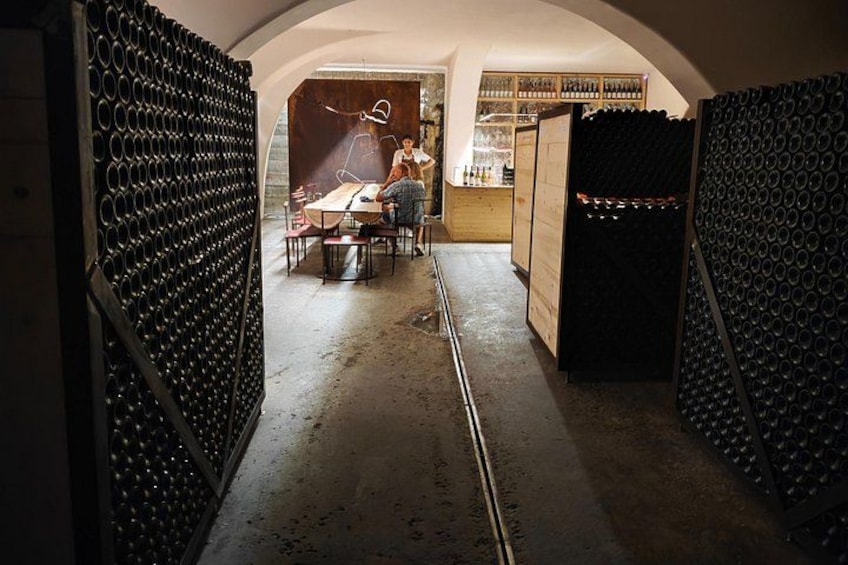 A wine cellar with rows of wine bottles, a wooden table, and a person standing by the table. 2