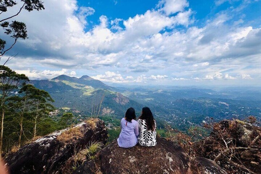 Two people sitting on a rocky outcrop overlooking a mountainous landscape. 4