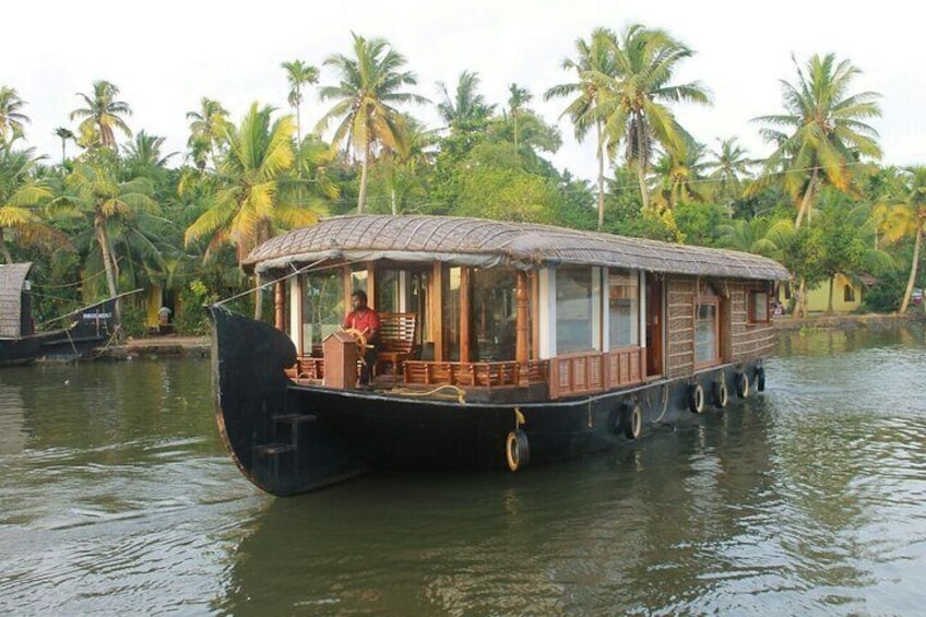 A traditional houseboat on water with a person inside, surrounded by palm trees. 1