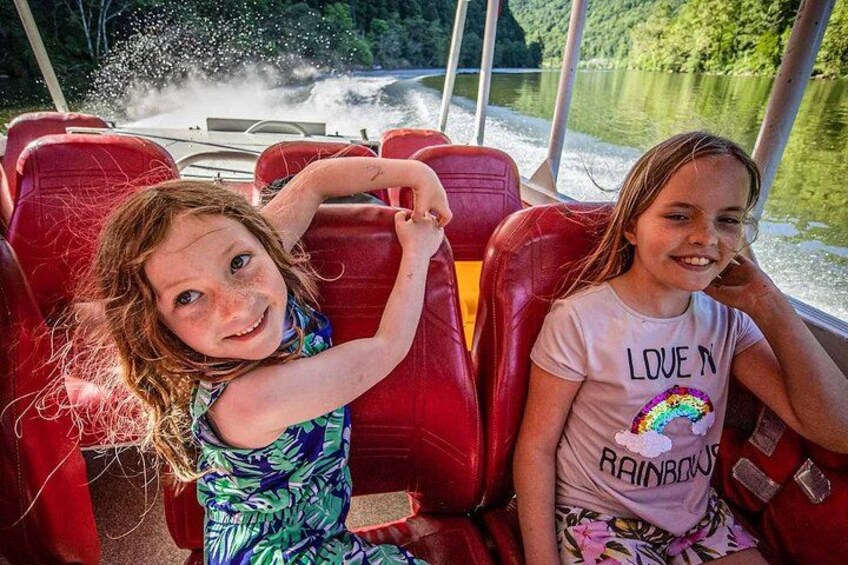 Zwei Kinder in einem Boot mit roten Sitzen, ein Kind trägt ein T-Shirt mit Regenbogenmuster, das andere ein Blumenkleid. 4