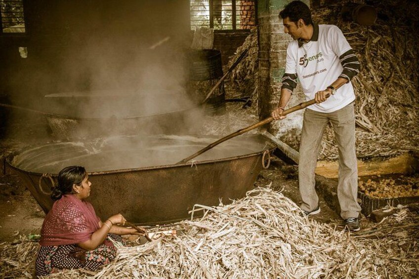 A person stirring a large metal pot over a fire, another person kneeling beside it, and a pile of straw on the ground. 2