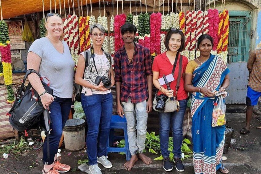 A group of people standing in front of a flower stall with various flowers on display. 3