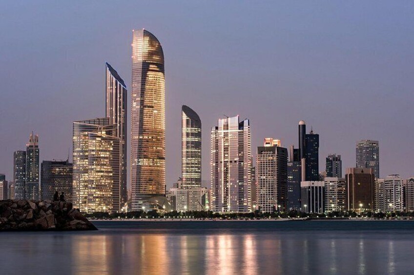A city skyline with modern skyscrapers, a body of water in the foreground, and a clear sky. 3